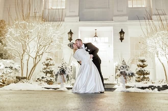 Couple kissing in front of The Commons 1854 in snow with fairy lights on trees