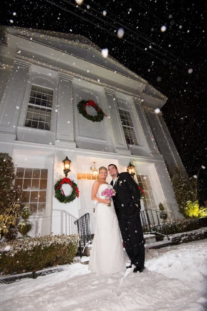 Couple in falling snow at night in front of The Commons 1854 with Christmas wreaths
