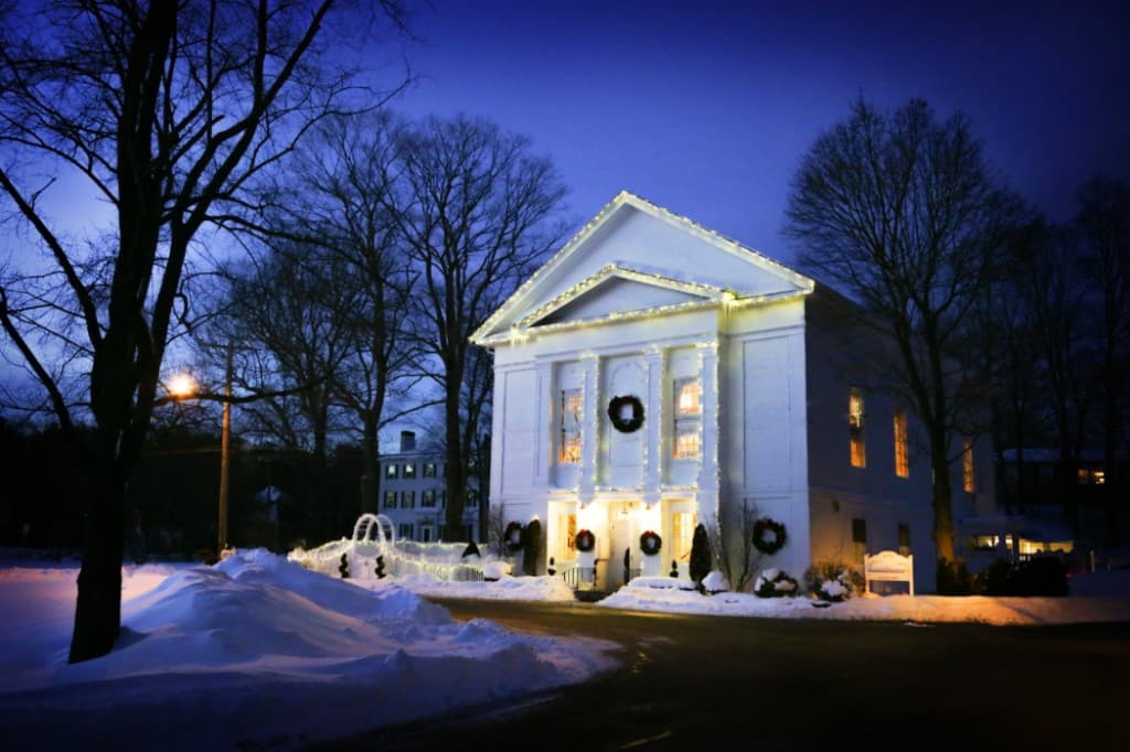 The Commons 1854 building lit up with Christmas lights and wreaths in winter snow — Topsfield Massachusetts